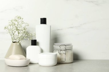 Banyo aksesuarları. Kişisel bakım ürünleri ve vazodaki alçıtaşı çiçekleri beyaz mermer duvarın yanındaki gri masada, metin için boşluk