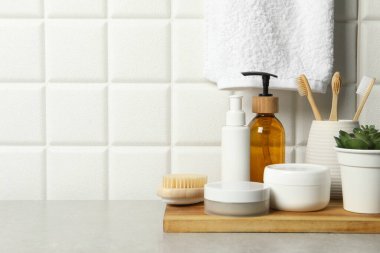 Farklı banyo aksesuarları ve kişisel bakım ürünleri beyaz fayanslı duvarın yanındaki gri masada, metin için yer var.