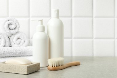 Farklı banyo aksesuarları ve kişisel bakım ürünleri beyaz fayanslı duvarın yanındaki gri masada, metin için yer var.