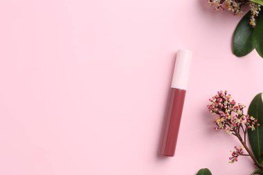 Pembe arka planda parlak dudak parlatıcısı ve çiçek açan dallar, üst manzara. Metin için boşluk