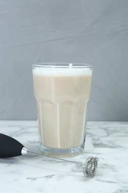 Mini mixer (milk frother) and tasty cappuccino in glass on white marble table clipart