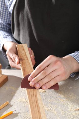 Gri masadaki zımpara kağıdıyla tahta cilalayan adam, yakın plan.