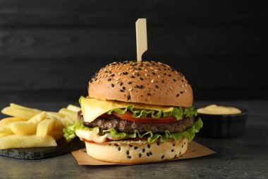 Lezzetli köfteli hamburger, patates kızartması ve gri masada koyu arkaplanda sos.