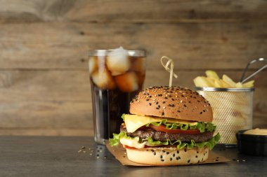 Lezzetli köfteli burger, soda, patates kızartması ve sos gri masada, mesaj için yer var.