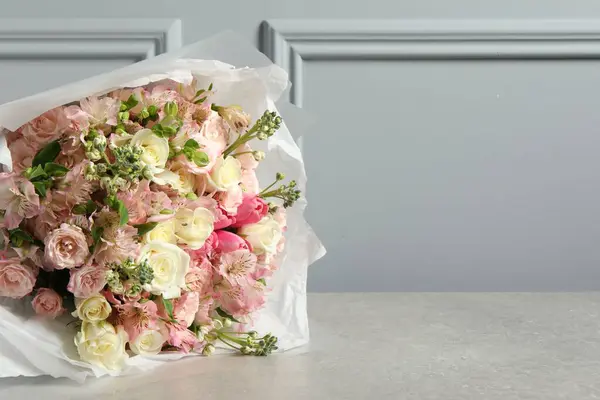 Beautiful bouquet of fresh flowers on table near grey wall, space for text