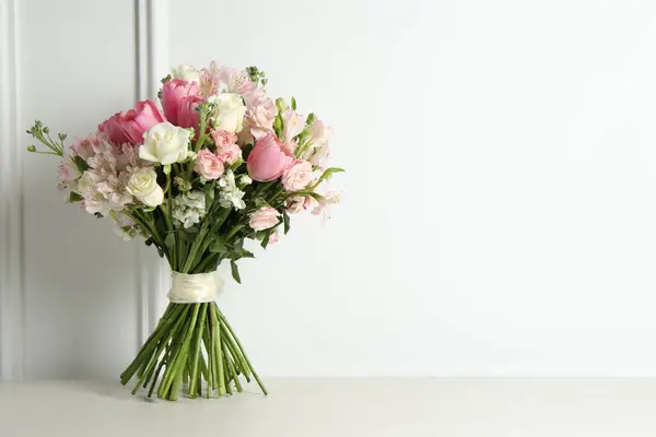 Beautiful bouquet of fresh flowers on table near white wall. Space for text