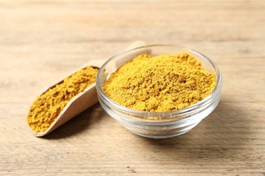 Curry powder in bowl and scoop on wooden table, closeup clipart