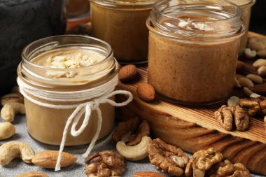 Tasty nut butters in jars and raw nuts on table, closeup clipart