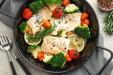 Gri masada servis edilen sebzelerle pişirilmiş lezzetli morina balığı.