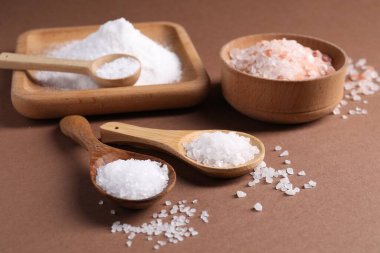 Kahverengi arka planda farklı bulaşık takımlarındaki doğal tuz, yakın plan.