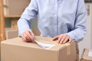 Paketleme. Postane çalışanı kapalı bir kutuya barkod yapıştırıyor.