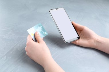 Çevrimiçi ödeme. Akıllı telefonu ve kredi kartı olan bir kadın beyaz masada, yakın plan.