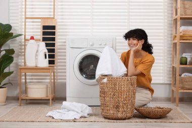 Çamaşır makinesinin yanında çamaşırları olan mutlu kadın.