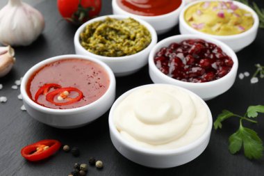 Farklı lezzetli soslar tabakta ve malzemeler siyah masada, yakın plan.