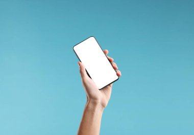 Açık mavi arka planda boş ekranlı akıllı telefon tutan adam, yakın plan. Tasarım için model