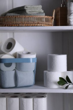 Tuvalet kağıdı ruloları, yeşil yapraklar ve beyaz raflarda havlular.