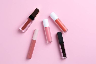 Pembe arka planda farklı dudak parlatıcıları, düz yatış