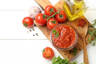 Kavanozda ev yapımı domates sosu, beyaz ahşap masa üzerinde kaşık ve taze malzemeler, düz yatak. Metin için boşluk