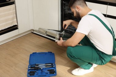 Görevli mutfakta tornavidayla bulaşık makinesinin kapısını tamir ediyor.