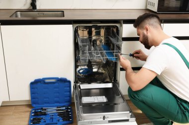 Görevli mutfakta bulaşık makinesini tornavidayla tamir ediyor.