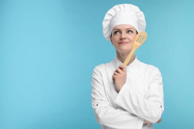 Üniformalı mutlu aşçı açık mavi arka planda ahşap spatula tutuyor, mesaj için yer var.