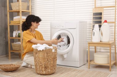 Çamaşır makinesine çamaşır koyan mutlu bir kadın.