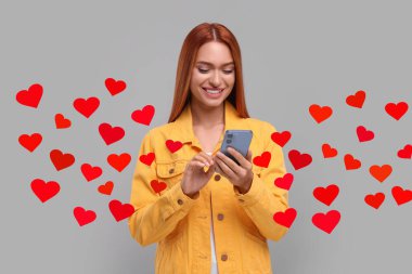 Şehirlerarası aşk. Gri arka planda akıllı telefondan sevgilisiyle sohbet eden bir kadın. Kalpler yerinden fırlıyor ve etrafında dönüp duruyor.