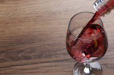 Ahşap masada cama lezzetli kırmızı şarap dökmek, yakın plan. Metin için boşluk