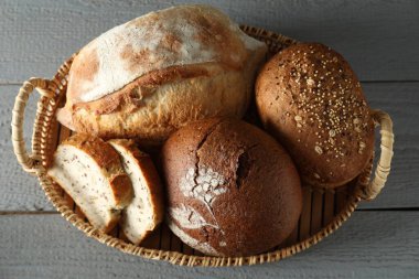 Gri ahşap masanın üzerinde değişik taze ekmek türleri olan sepet, üst manzara.