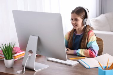 E-öğrenme. İçerideki masada online ders sırasında bilgisayar ve kulaklık kullanan tatlı bir kız.