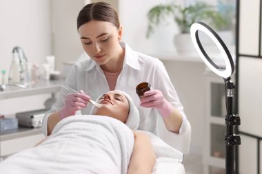 Kozmetik uzmanı klinikte kadının yüzüne maske takıyor.