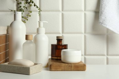 Duvarın yanındaki beyaz masada farklı banyo aksesuarları ve kişisel bakım ürünleri var.