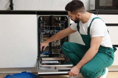 Görevli mutfakta tornavidayla bulaşık makinesinin kapısını tamir ediyor.