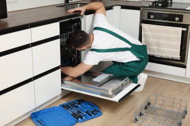 Mutfaktaki alet çantasının yanında bulaşık makinesini tamir eden bir tamirci.