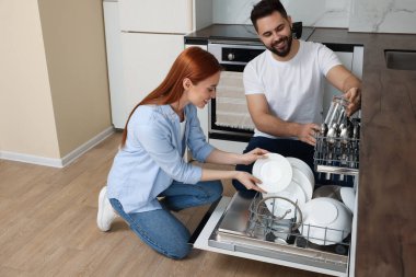 Mutfakta bulaşık makinesini tabakla dolduran mutlu çift.