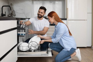 Mutfakta bulaşık makinesini tabakla dolduran mutlu çift.