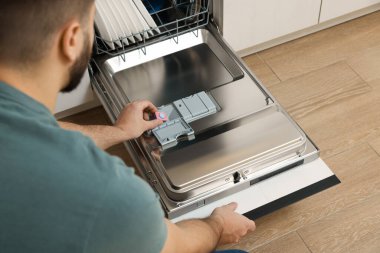 Adam bulaşık makinesine deterjan koyuyor, yakın plan.