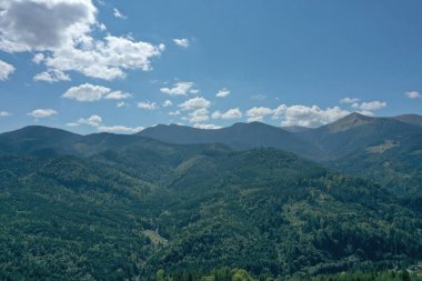 Güneşli bir günde mavi gökyüzünün altında yeşil ağaçlarla güzel bir dağ manzarası. Drone fotoğrafçılığı