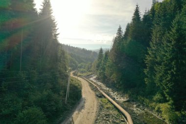 Dağlardaki yeşil ağaçların arasında toprak yol boyunca uzanan nehirle güzel bir manzara. Drone fotoğrafçılığı