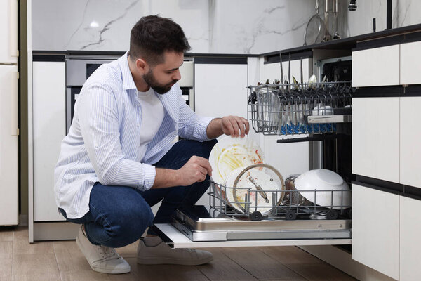 Man loading dishwasher with dirty plates indoors