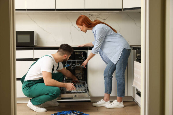 Woman looking how serviceman repairing her dishwasher in kitchen
