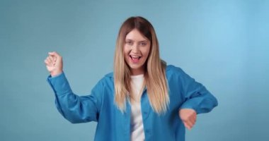 Açık mavi arka planda dans eden mutlu genç kadın