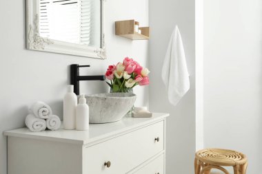 Güzel pembe laleleri ve banyo lavabosunun yanında tuvalet eşyaları olan vazo.
