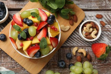 Lezzetli meyve salatası kasede ve ahşap masada malzemeler var.