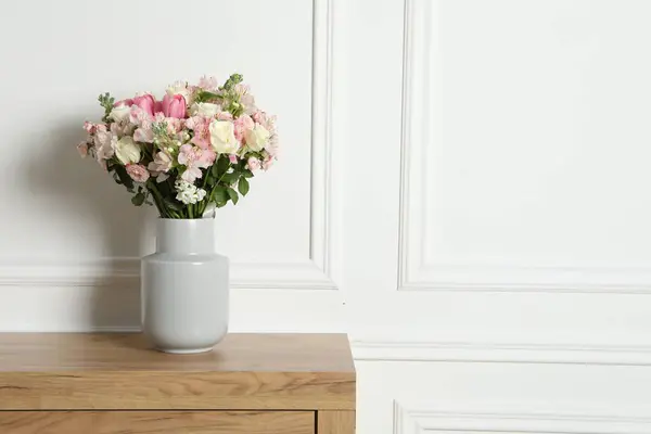 Beautiful bouquet of fresh flowers in vase on wooden table near white wall, space for text