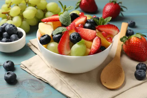 味道鲜美的水果沙拉放在碗里 配料和勺子放在浅蓝色的木桌上 特写镜头 — 图库照片