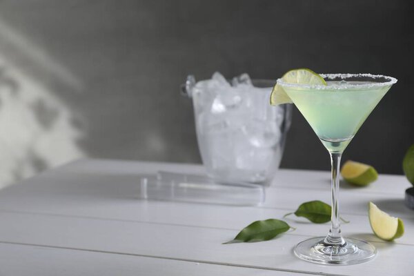Delicious Margarita cocktail in glass and lime on white wooden table, space for text