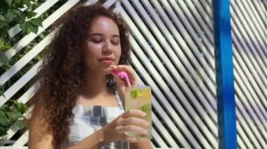 Güzel genç bir kadın açık kafede ferahlatıcı limonata içiyor. Düşük açılı. Yavaş çekim etkisi