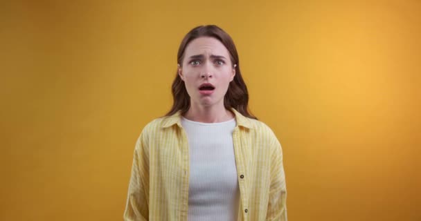 一个情绪化的年轻女人在黄色背景下看到了可怕的东西 — 图库视频影像