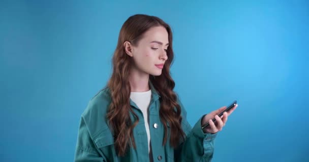 快乐的年轻女人拿着手机得到了快乐的消息 浅蓝色背景 免版税图库视频